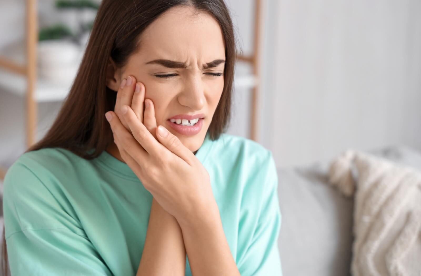 Person grimacing in pain holding their cheek indicating a toothache or dental discomfort
